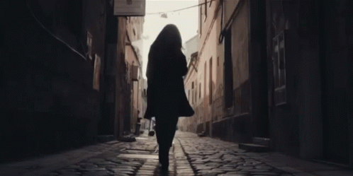 A Woman Walking Down A Cobblestone Street With A Sign That Says ' A Few Steps ' On It GIF