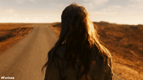 A Woman Walking Down A Dirt Road With The Hashtag #Furiosa On The Bottom GIF