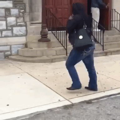 A Woman Walking Down A Sidewalk With A Purse On Her Back GIF
