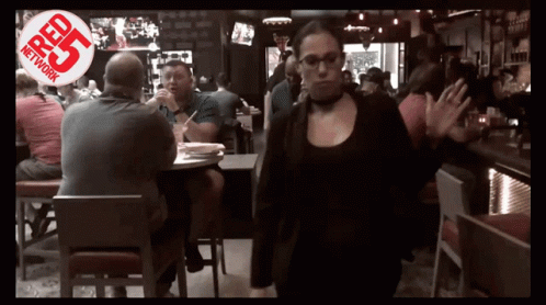 a woman walking through a crowded restaurant with a red r25 network logo behind her