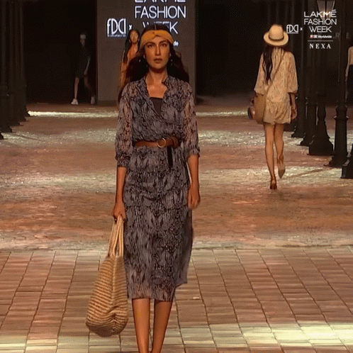 A Woman Walks Down A Runway At A Fashion Show GIF