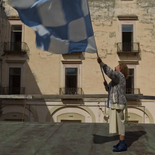 A Woman Waves A Blue And White Flag In Front Of A Building GIF