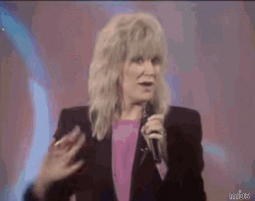 A Woman Waving Her Hand While Holding A Microphone With Mbs Written Below Her GIF