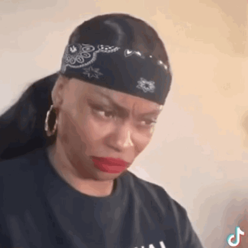 a woman wearing a bandana and earrings is making a sad face .