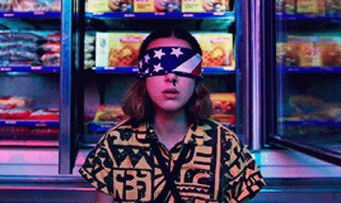 A Woman Wearing A Bandana With An American Flag On Her Eyes Is Standing In Front Of A Refrigerator . GIF