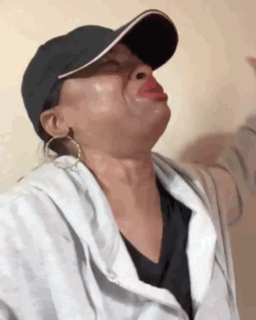 a woman wearing a baseball cap and earrings is making a face .