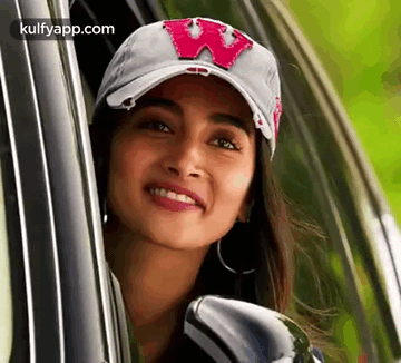 A Woman Wearing A Baseball Cap Is Looking Out Of A Car Window . GIF