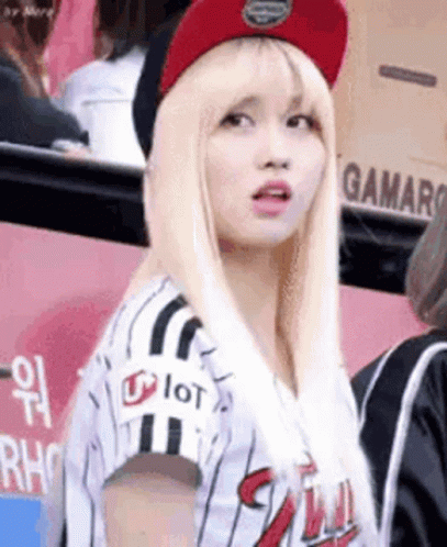 A Woman Wearing A Baseball Uniform And A Red Hat Is Standing In A Crowd . GIF
