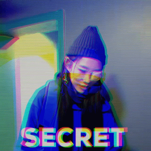 A Woman Wearing A Beanie And Sunglasses Is Standing In Front Of The Word Secret GIF