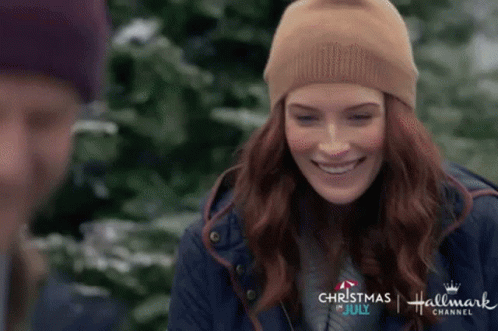 A Woman Wearing A Beanie Is Smiling In Front Of A Man In A Blue Jacket . GIF