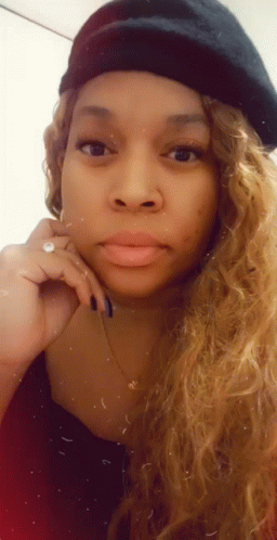 A Woman Wearing A Beret And A Necklace Is Looking At The Camera . GIF