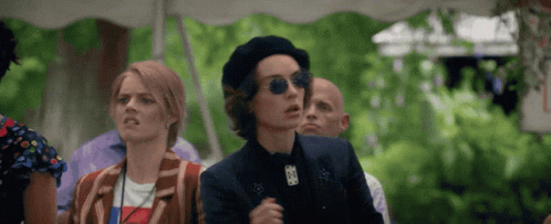 A Woman Wearing A Beret And Sunglasses Stands In A Crowd GIF