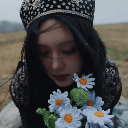 A Woman Wearing A Black And White Polka Dot Hat Holds A Bouquet Of Crocheted Daisies GIF