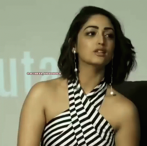 A Woman Wearing A Black And White Striped Dress And Earrings Is Looking At The Camera . GIF