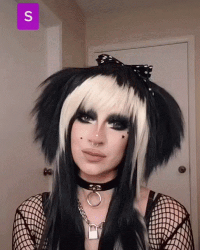 A Woman Wearing A Black And White Wig And A Choker With The Letter S On The Bottom GIF