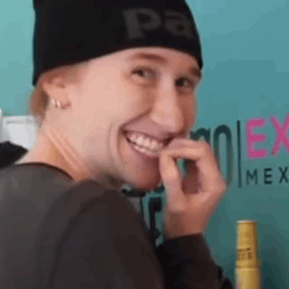 a woman wearing a black beanie is smiling and biting her finger .