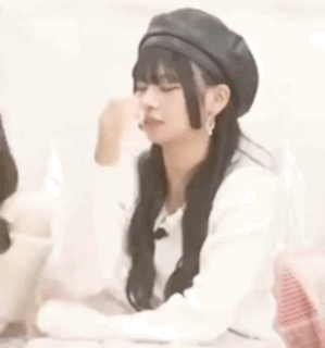 A Woman Wearing A Black Beret Is Sitting At A Table With Her Eyes Closed . GIF