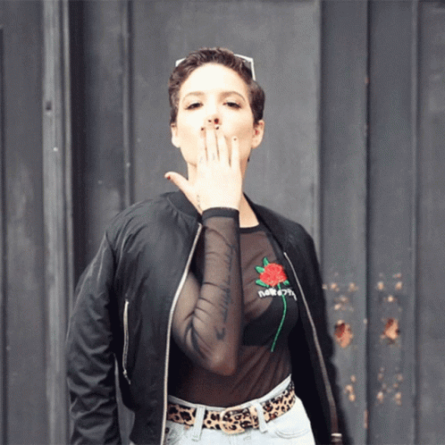 A Woman Wearing A Black Bomber Jacket And A Sheer Top With A Rose On It GIF