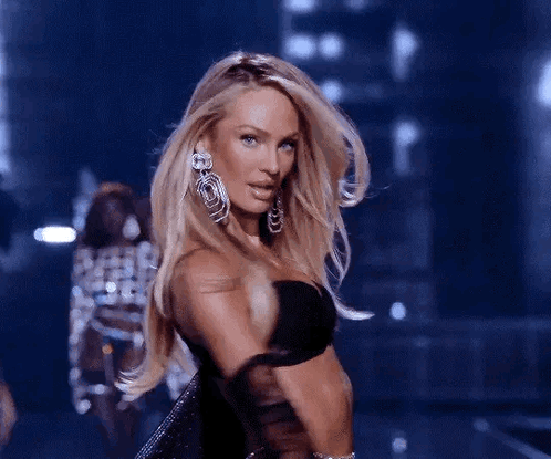 A Woman Wearing A Black Bra And Earrings Is Walking Down A Runway . GIF