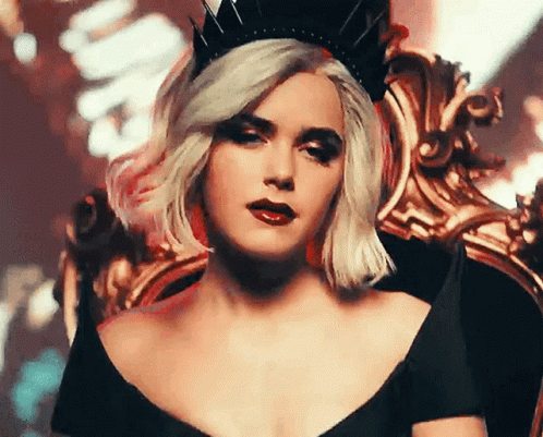 A Woman Wearing A Black Dress And A Crown Is Sitting In A Chair . GIF