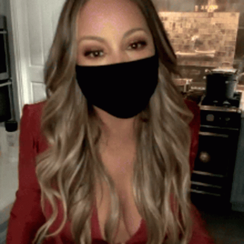 A Woman Wearing A Black Face Mask Is Sitting In A Kitchen GIF