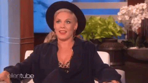 A Woman Wearing A Black Hat And A Black Jacket Is Sitting In A Chair On A Show . GIF