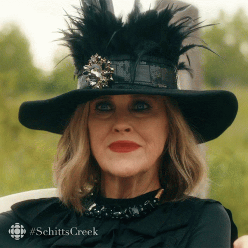 A Woman Wearing A Black Hat And A Black Shirt With #Schitts Creek Written On The Bottom GIF