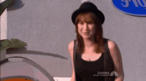 A Woman Wearing A Black Hat And A Black Tank Top Stands In Front Of A Sign That Says 3Kawa GIF