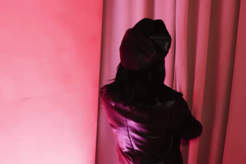 a woman wearing a black hat and a leather jacket is standing in front of a pink curtain
