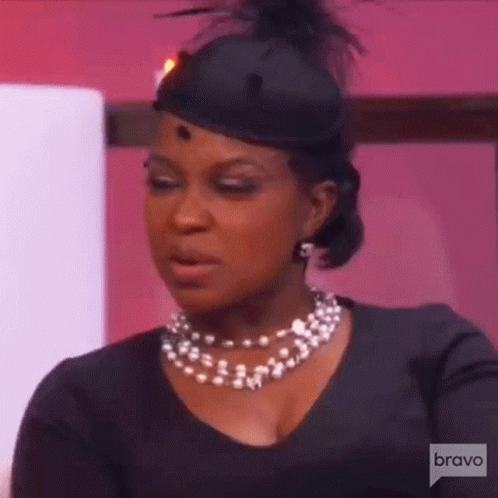A Woman Wearing A Black Hat And A Pearl Necklace . GIF