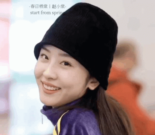 A Woman Wearing A Black Hat And A Purple Sweater Smiles For The Camera GIF