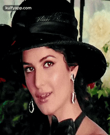 A Woman Wearing A Black Hat And Earrings Is Smiling For The Camera . GIF