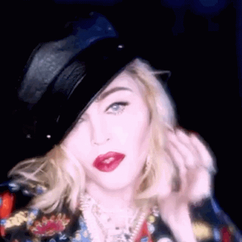 A Woman Wearing A Black Hat And Red Lipstick Is Looking At The Camera . GIF