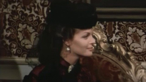 A Woman Wearing A Black Hat Is Sitting On A Bed GIF