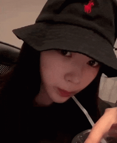 A Woman Wearing A Black Hat With A Red Horse On It Is Drinking Through A Straw . GIF