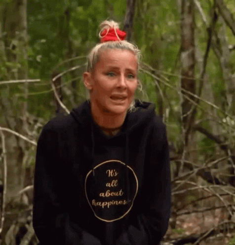 A Woman Wearing A Black Hoodie That Says `` It 'S All About Happiness '' Is Sitting In The Woods . GIF