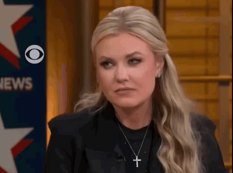 A Woman Wearing A Black Jacket And A Cross Necklace Is Sitting In Front Of A News Sign . GIF