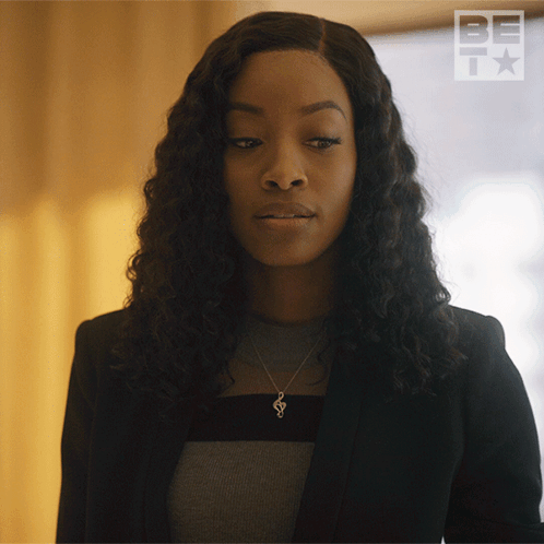 A Woman Wearing A Black Jacket And A Necklace With A S On It GIF