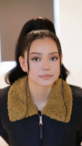 A Woman Wearing A Black Jacket With A Furry Collar Looks At The Camera GIF