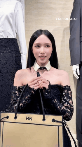 a woman wearing a black lace off the shoulder top is holding a bag with the letter mn on it