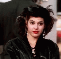 A Woman Wearing A Black Leather Jacket And A Hat Is Looking At The Camera . GIF