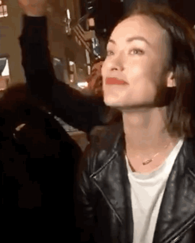 A Woman Wearing A Black Leather Jacket And A White T-Shirt Is Smiling And Looking Up . GIF