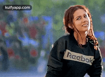 A Woman Wearing A Black Reebok Sweatshirt Is Smiling And Looking Up . GIF