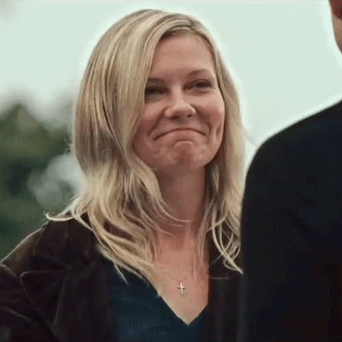 A Woman Wearing A Black Shirt And A Cross Necklace Is Smiling While Looking At A Man . GIF