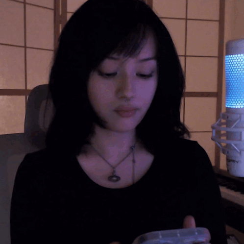A Woman Wearing A Black Shirt And A Necklace Is Sitting In Front Of A Microphone That Says ' Sven ' GIF