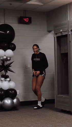 A Woman Wearing A Black Shirt That Says Las Vegas Basketball Is Standing In Front Of Balloons GIF