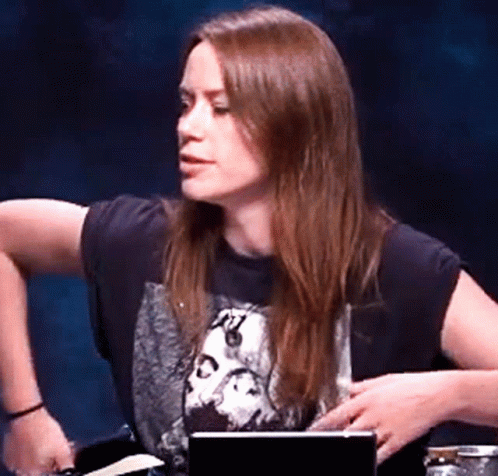 A Woman Wearing A Black Shirt With A Picture Of A Skull On It Is Sitting At A Table With A Laptop . GIF