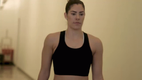 A Woman Wearing A Black Sports Bra Is Walking Down A Hallway GIF
