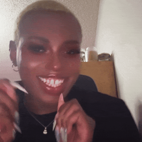 A Woman Wearing A Black Sweater And A Necklace Is Smiling GIF