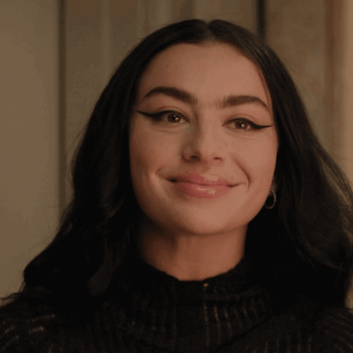 A Woman Wearing A Black Sweater And Hoop Earrings Smiles For The Camera GIF